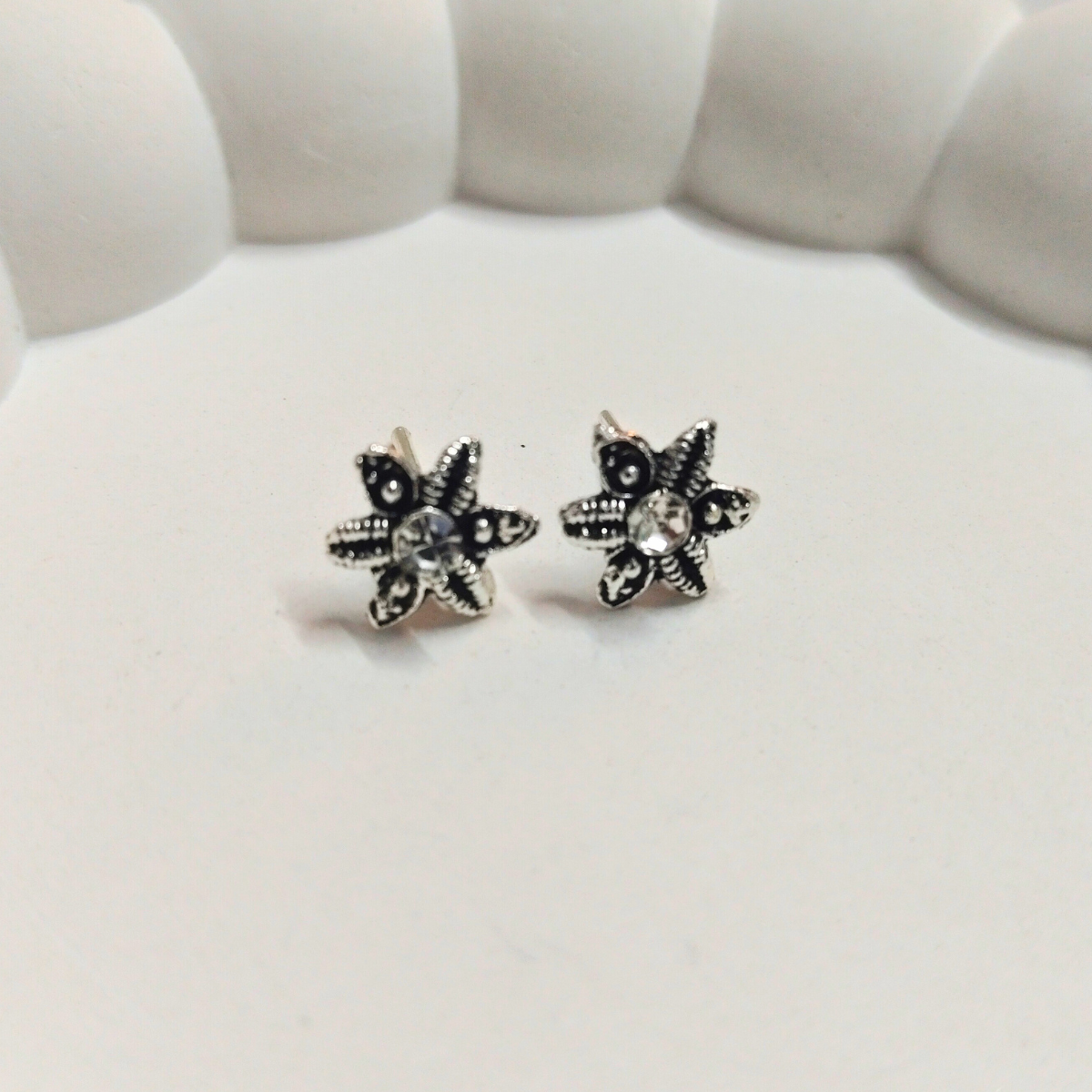 Antique silver six-petal floral stud earrings with detailed texture and crystal center on a white background
