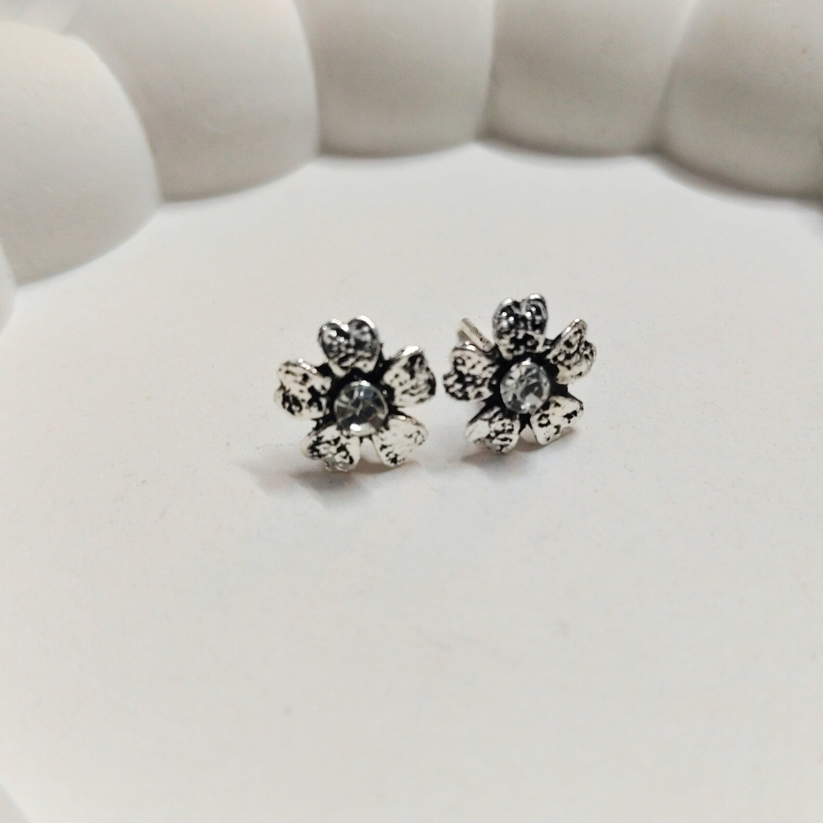 Antique silver flower stud earrings with textured petals and a crystal center on a soft white background