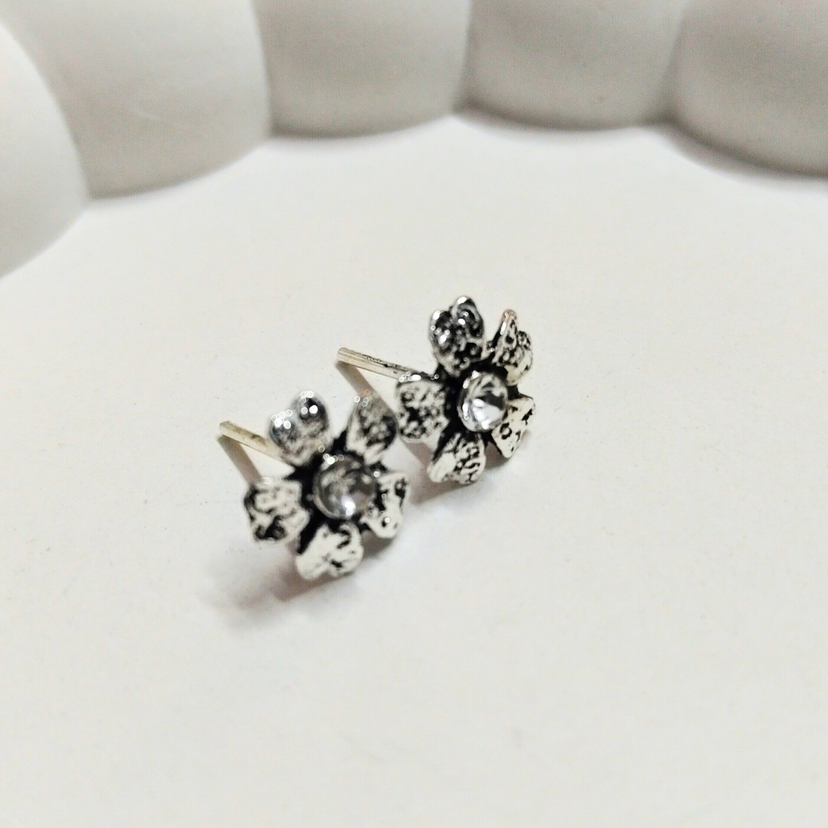 Close-up of vintage-style silver flower stud earrings with clear crystal center on a soft white background