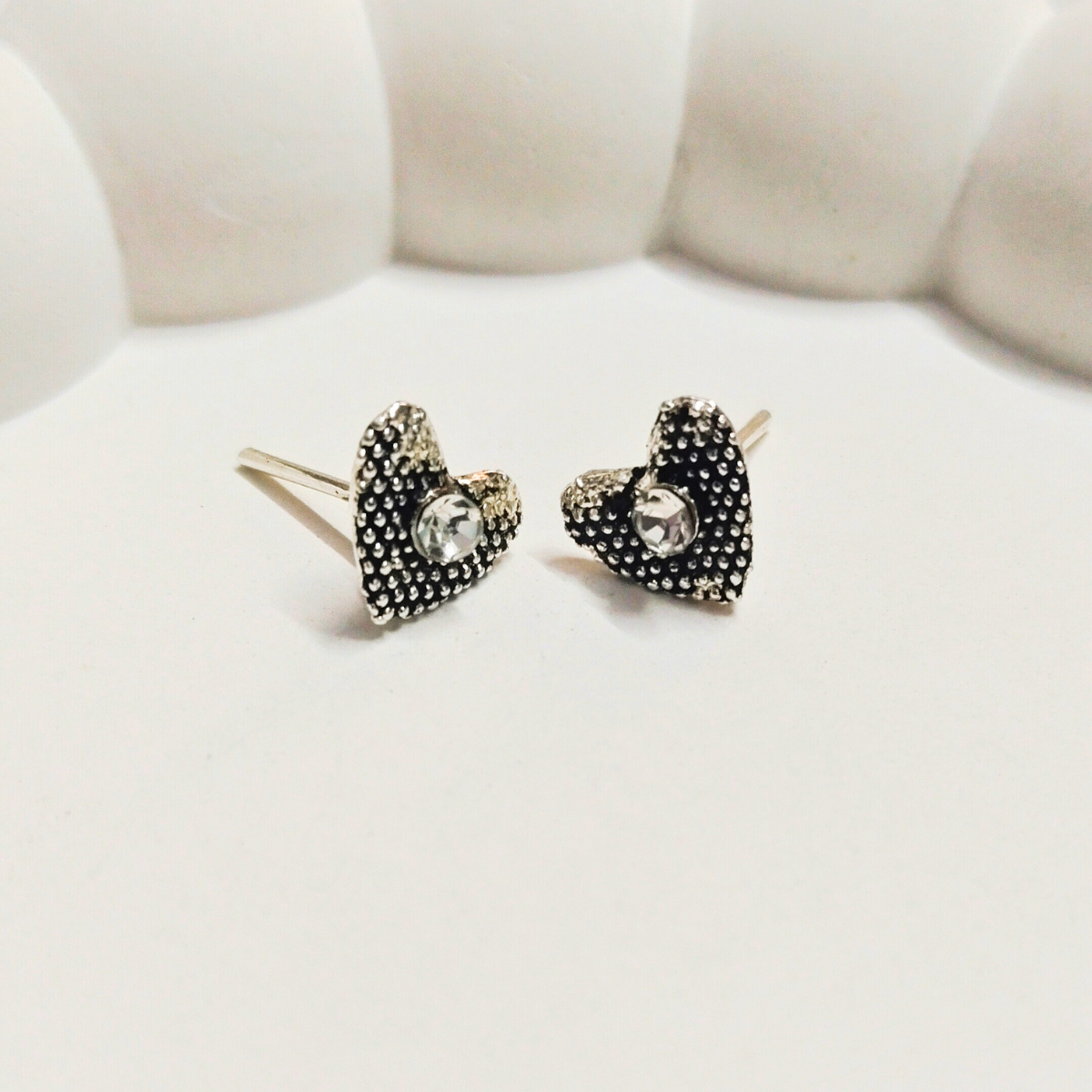 Antique heart-shaped stud earrings with crystal center on a white cushioned background