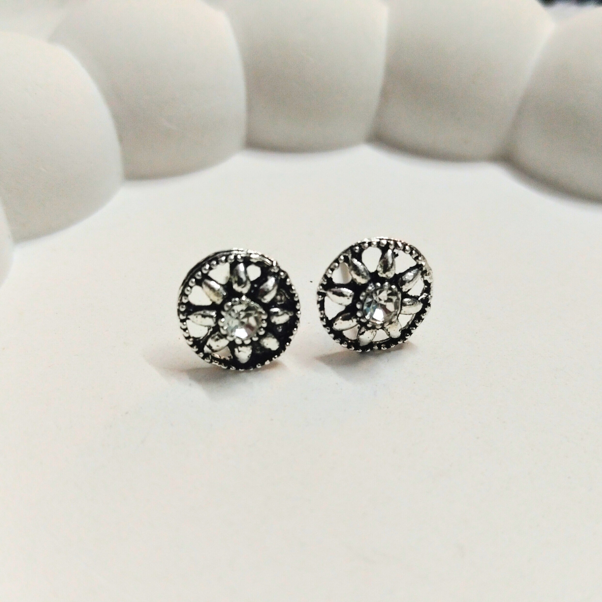 Antique silver round stud earrings with floral-inspired design and a central crystal on a white background