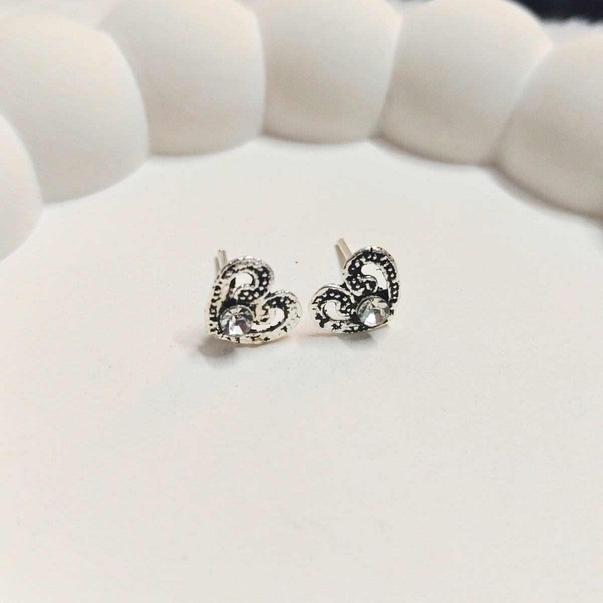 Antique heart-shaped stud earrings with filigree detailing and a central crystal on a white background
