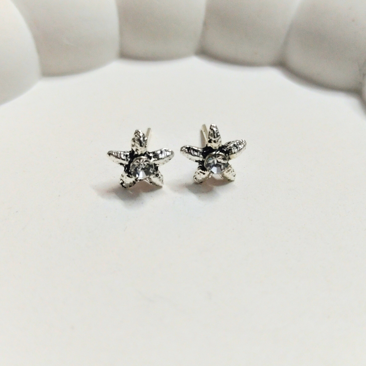 Antique silver star-shaped stud earrings with textured finish and clear crystal center on a white background