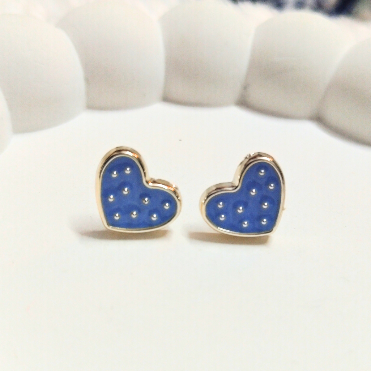 Blue heart-shaped stud earrings with white polka dots and gold border on a soft white surface