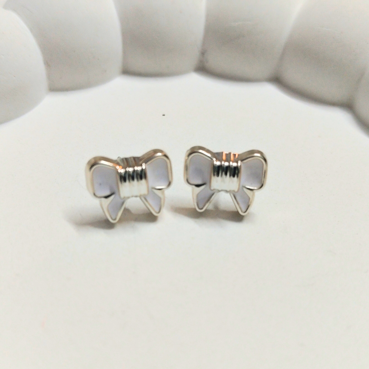 White bow-shaped stud earrings with gold border placed on a soft white surface