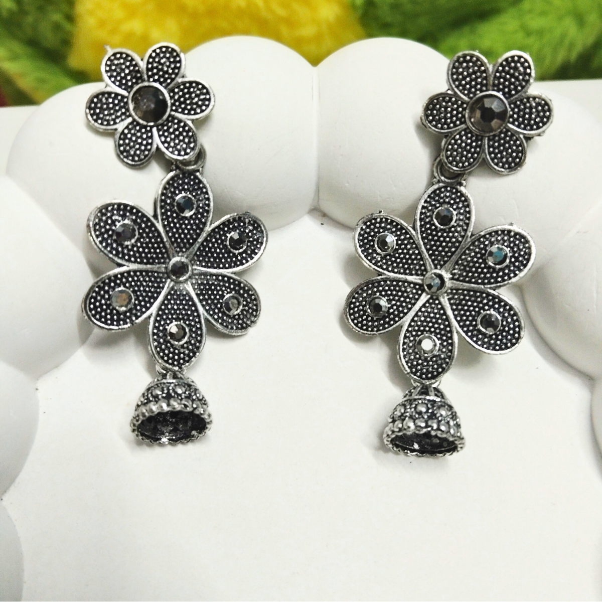 Pair of oxidized silver floral earrings with black stones and jhumka danglers placed on a white display with fur background.