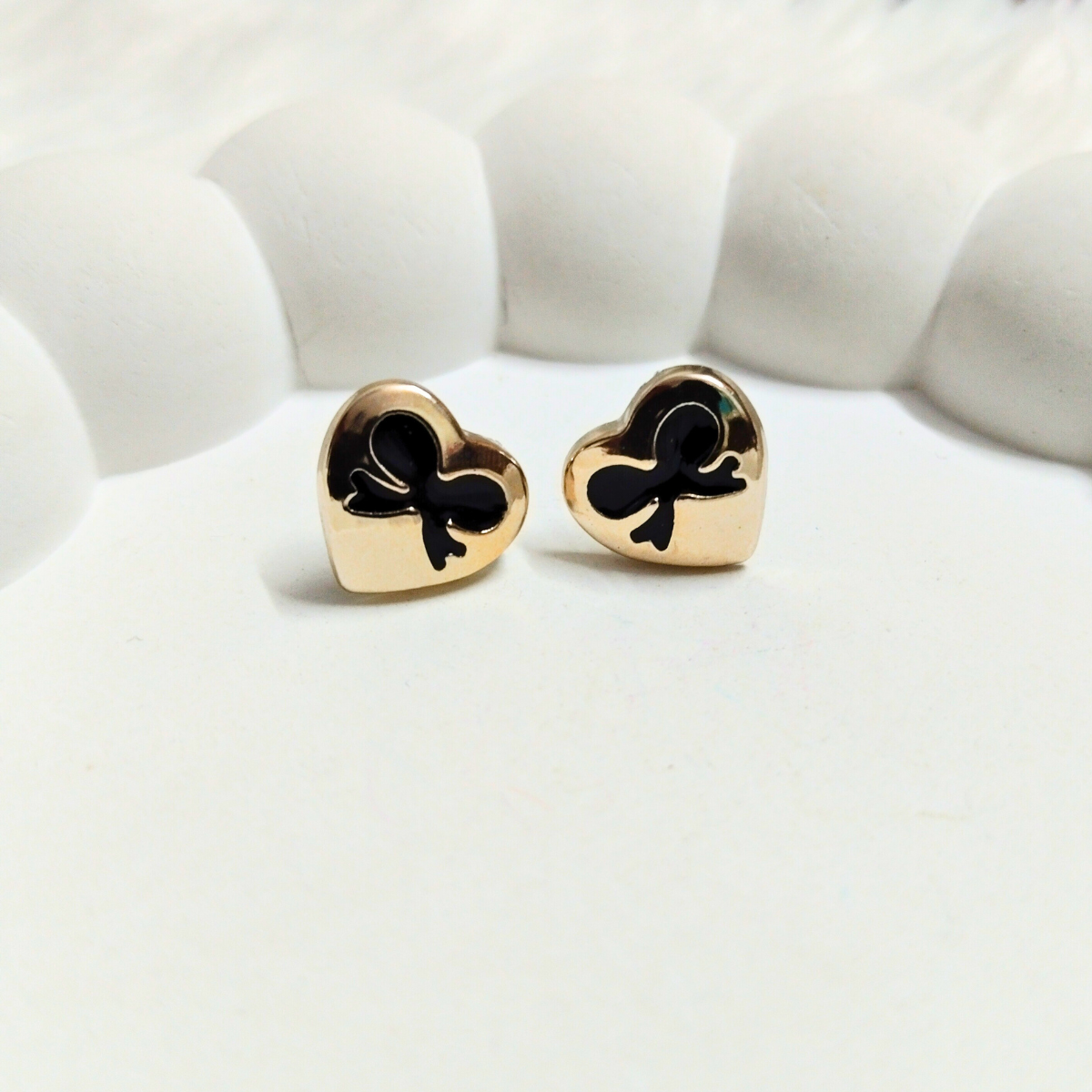 Gold heart stud earrings with black bow design on a white background