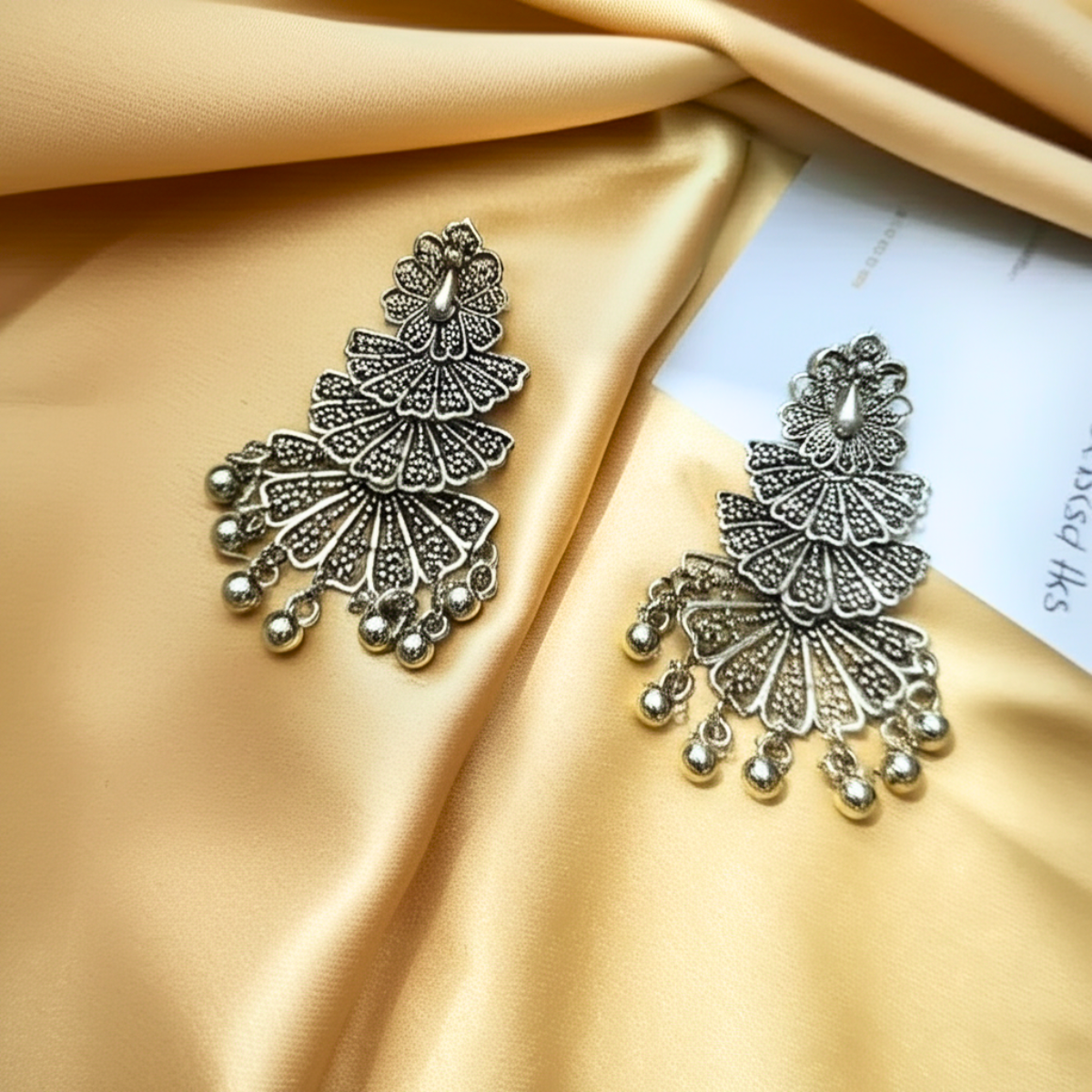 Oxidized silver peacock design earrings with intricate detailing and hanging beads on a white fur background.
