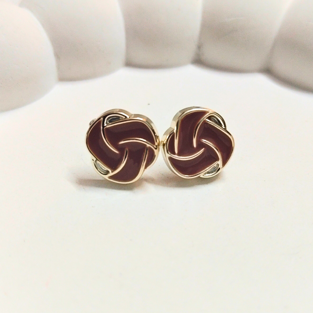 Red swirl stud earrings with gold outlining, shaped like a knotted spiral, displayed on a white surface