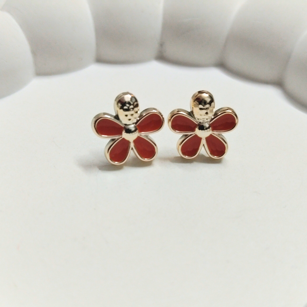 Red flower-shaped stud earrings with gold center and border placed on a white background