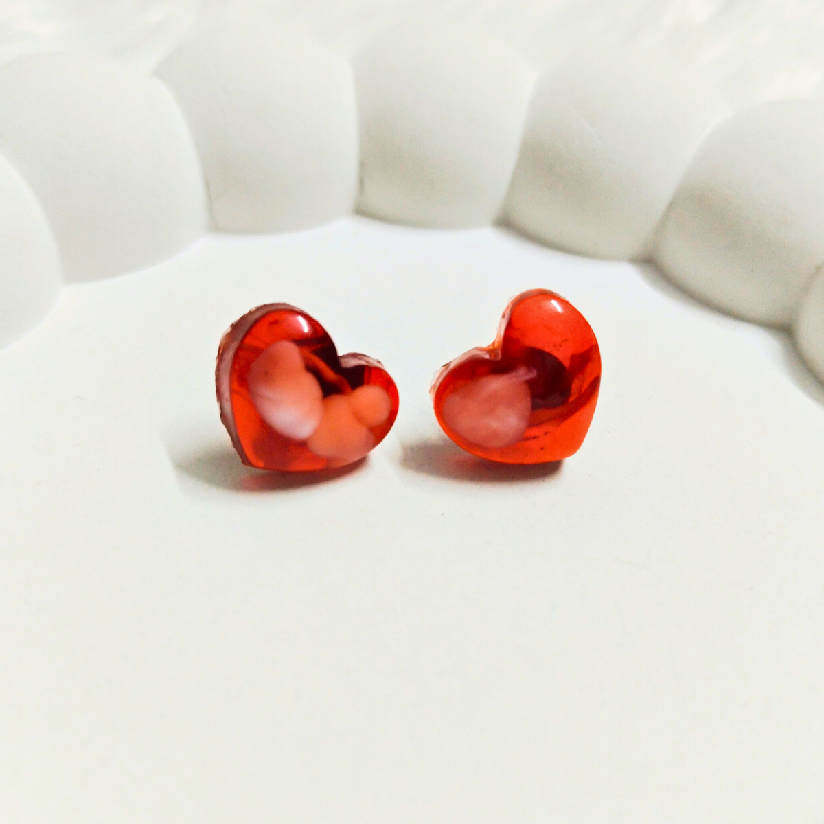 Red heart-shaped earrings with abstract white paint-like design on a white background