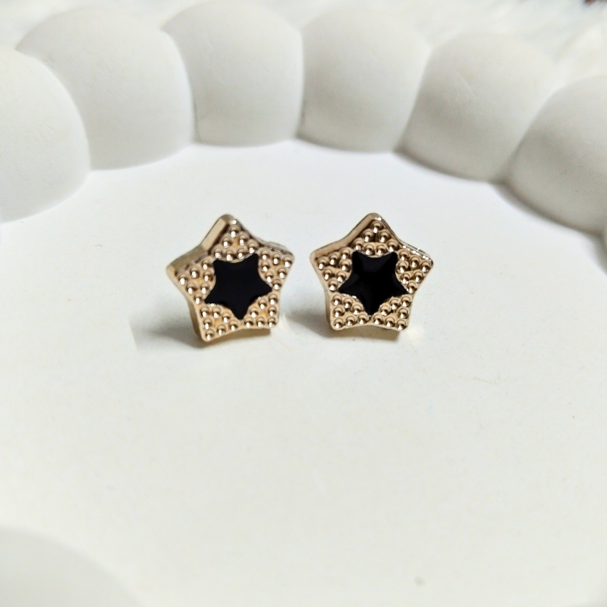 Gold star-shaped stud earrings with black enamel center on a white decorative surface