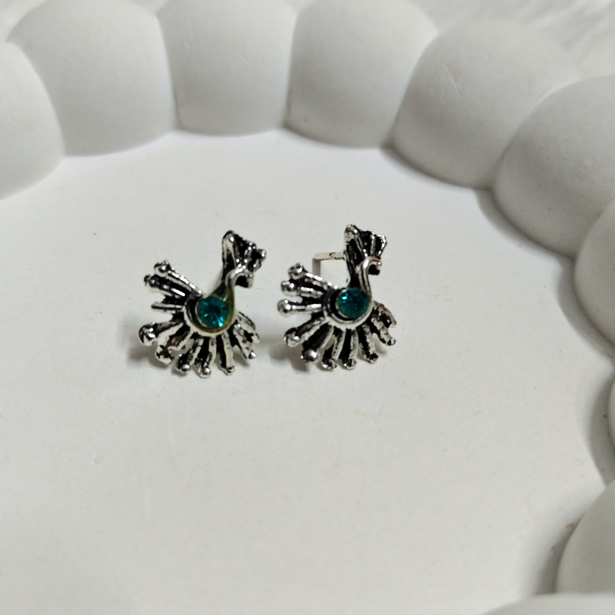 Silver peacock design stud earrings with teal stone center placed on a white background