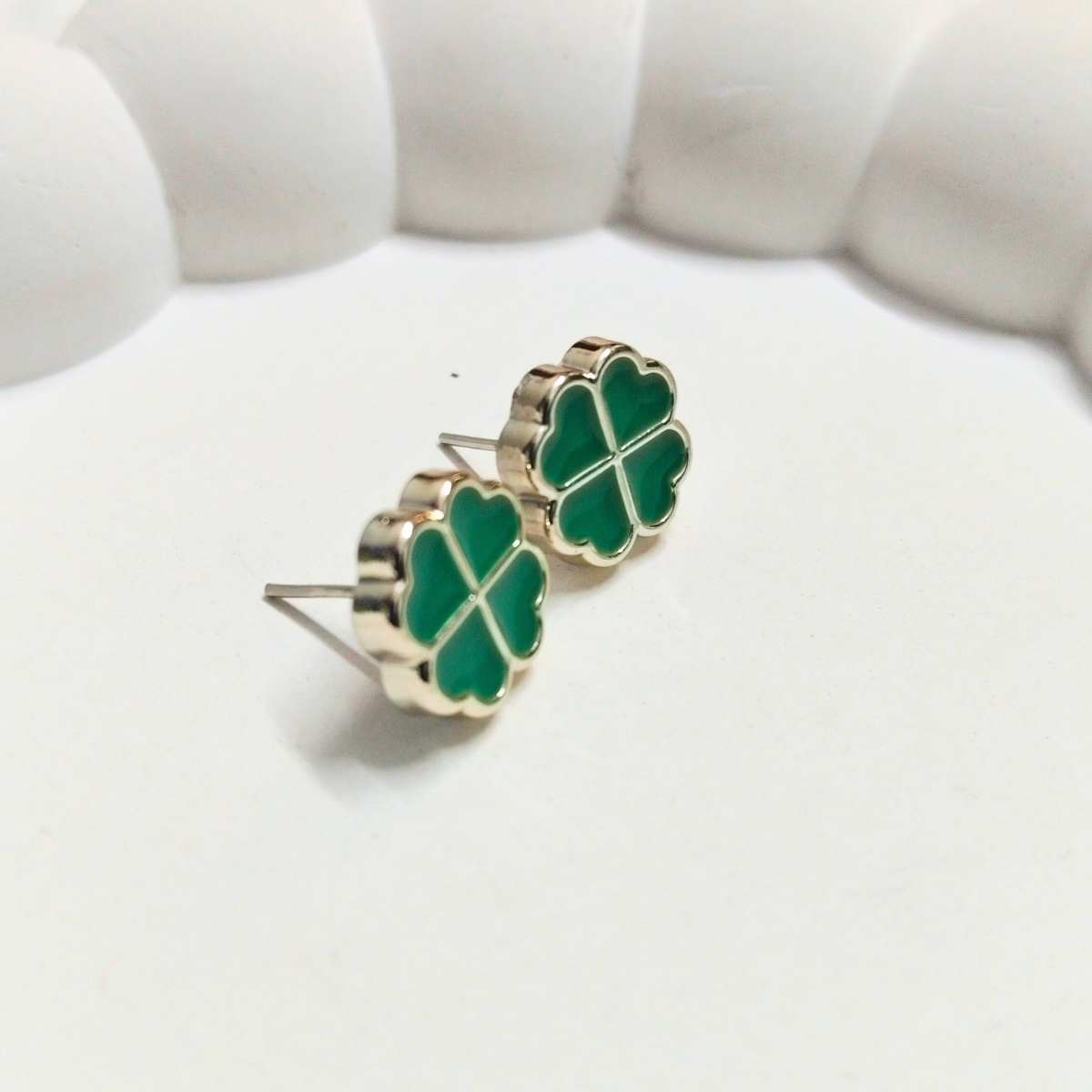 Green four-leaf clover stud earrings with gold outline on white background
