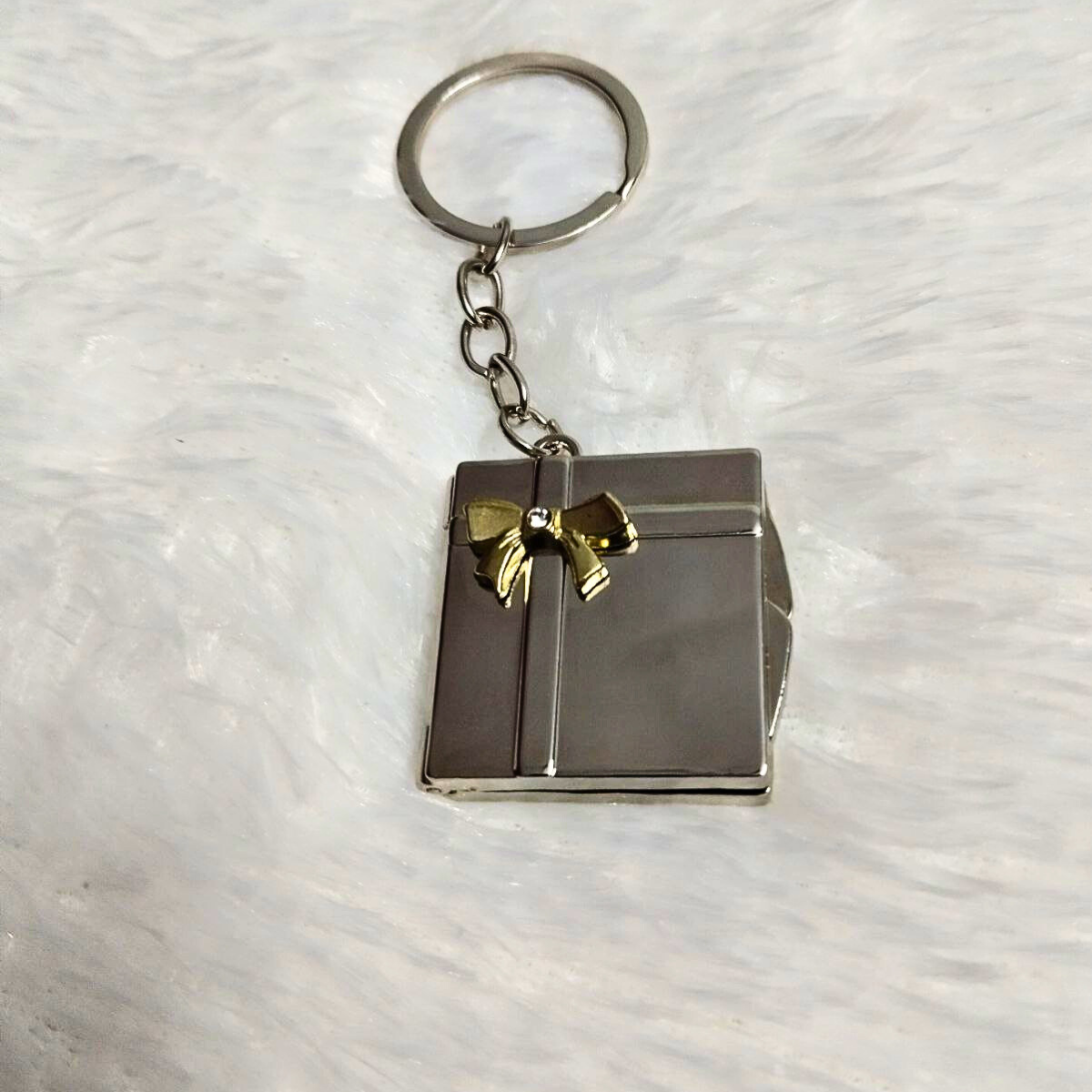 Closed book-shaped metal photo keychain with golden ribbon detail on a white background