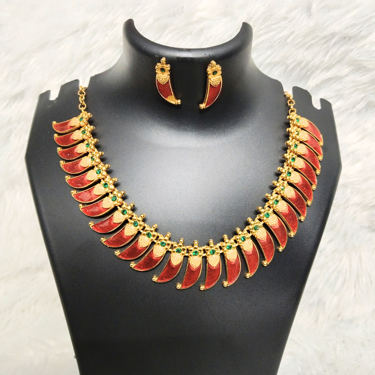 Gold plated red Palakka choker necklace set with enamel leaf design, green stone accents, and matching earrings, displayed on a black mannequin.