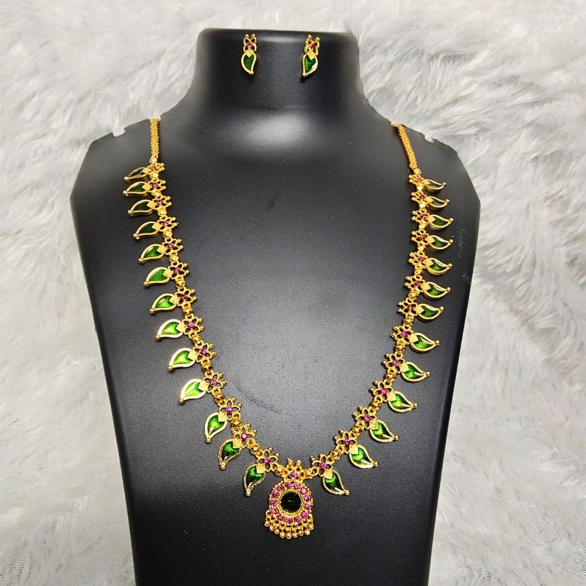 Gold plated traditional Palakka design necklace set with green leaf-shaped stones and pink floral accents, displayed on a black mannequin with earrings.